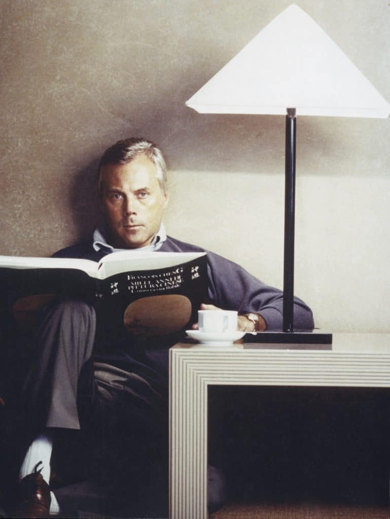Giorgio Armani reads a book next to his iconic Logo Lamp.