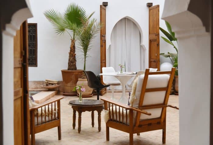 Eero Saarinen tulip chairs and table, vintage timber armchairs and palm trees in terracotta pots in the courtyard of Riad UP, Marrakech.