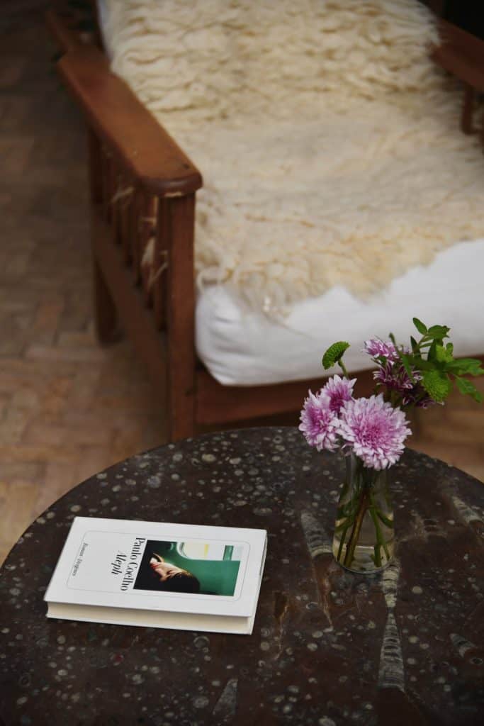 Riad UP. Sheepskin on vintage timber armchair, marble-top table and a vase of fresh dahlias in the courtyard of Riad UP, Marrakech.