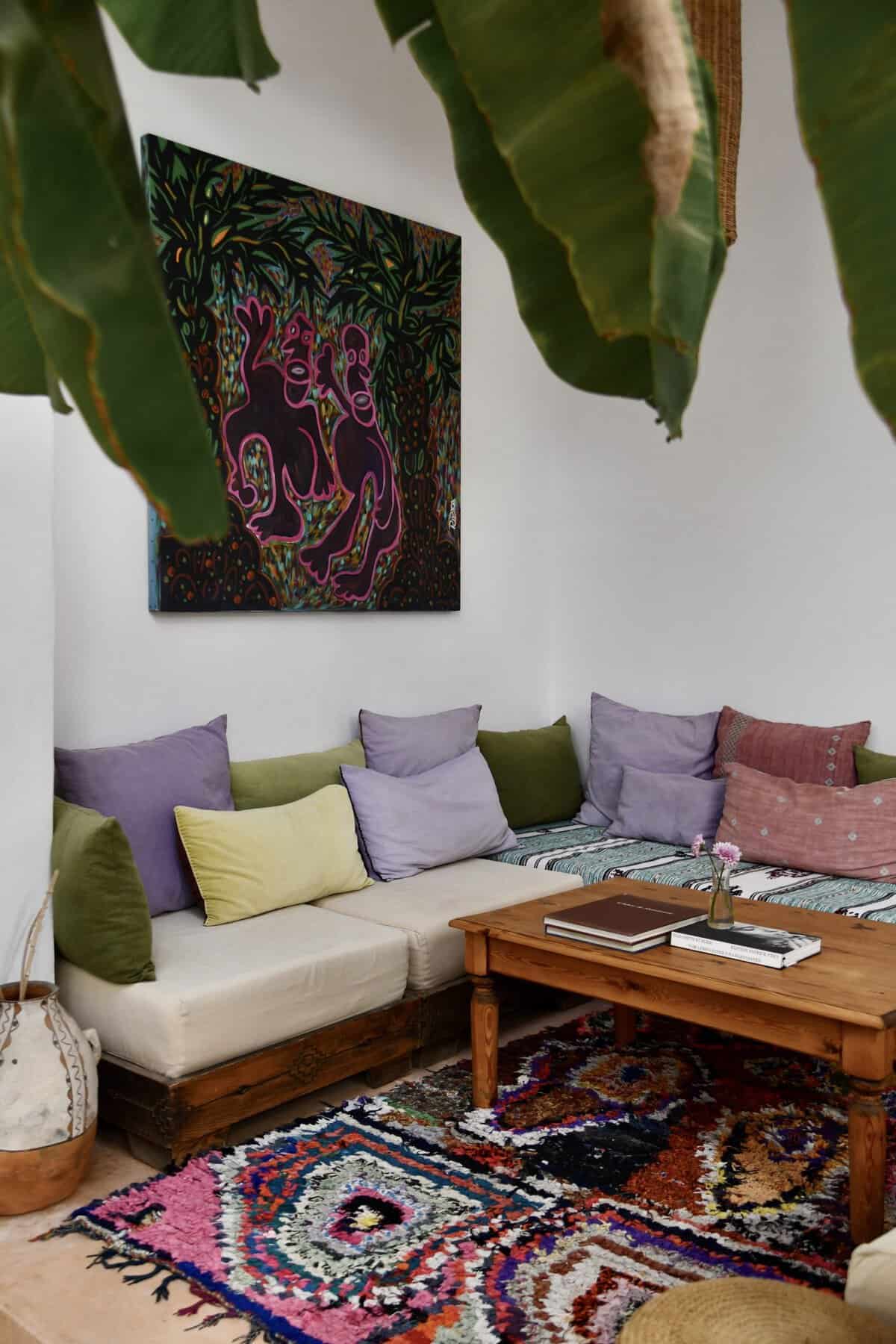 Riad UP. Banquette seating with olive, lilac and rose-coloured cushions, a boucherouite rag rug and painting by Indonesian artist Ribka Chanson-Hendriks in the courtyard lounge of Riad UP, Marrkaech.