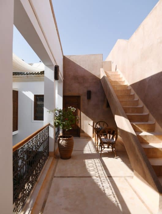 Terrace with tadelakt floor, rammed-earth walls, cane table and chairs, pot of white bougainvillea and staircase to roof, Riad UP, Marrakech.