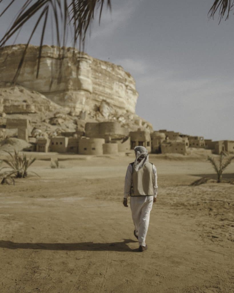 An Egyptian man with the vernacular eco architecture and desert landscape of Adrere Amellal, Siwa.